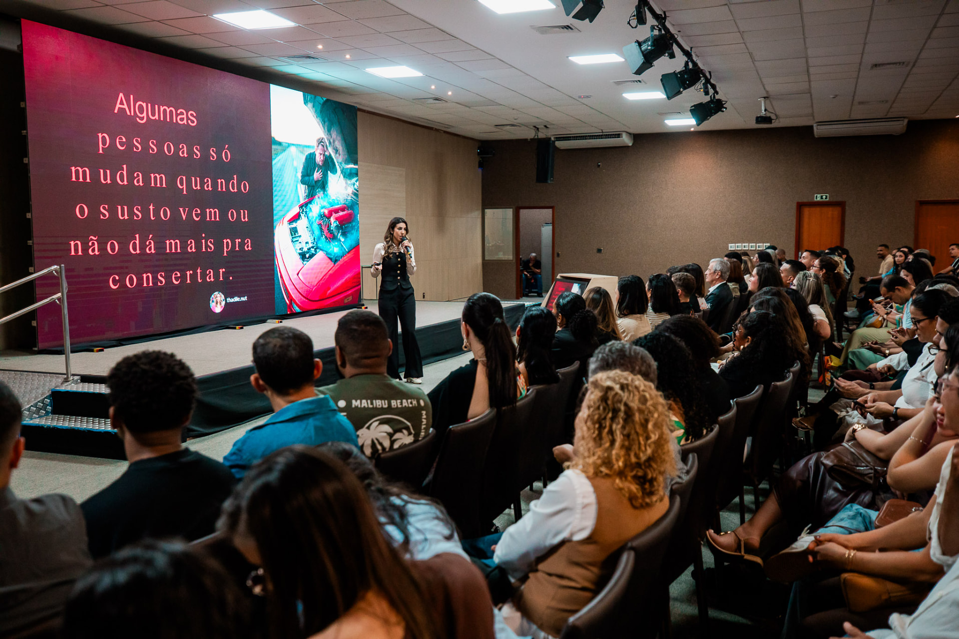 Thádile Thays Aguiar palestrando no palco para uma plateia cheia