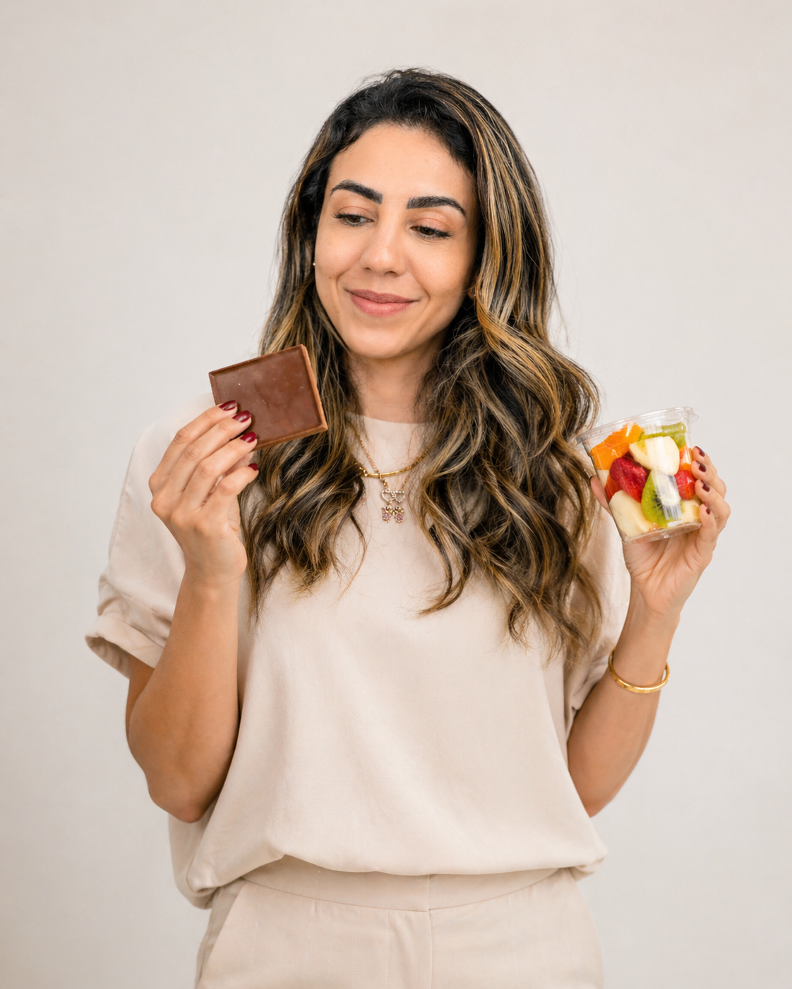 Thádile Thays Aguiar segurando um chocolate em uma mão e um pote de frutas na outra